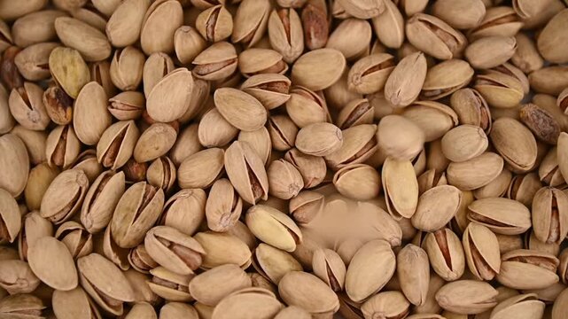 Pistachio nuts pouring and tumbling into pile on tabletop