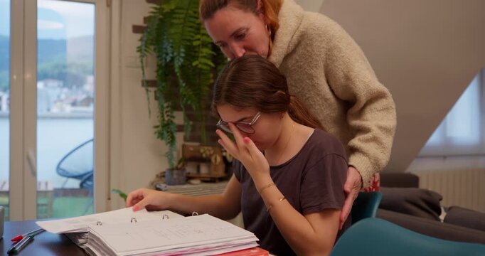 Overcoming Challenges: A compassionate figure offers comfort to a girl struggling with her studies. The scene, bathed in soft interior light, captures the delicate balance of support and resilience.