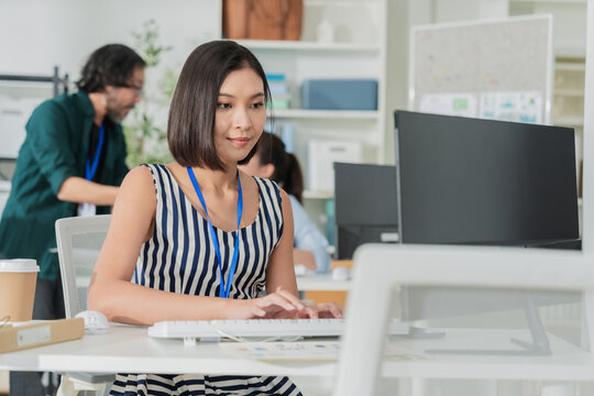 Young Asian businesswoman working on laptop in modern office, concentrated female employee typing on computer at creative workspace