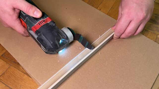 Close up of adult hands cutting laminate flooring plank with oscillating multitool, home renovation workspace on wooden floor, diy installation and carpentry detail