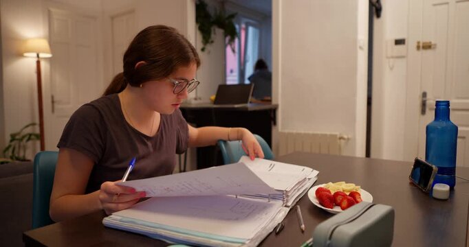 Focused Study: A young woman diligently engrossed in academic work, meticulously reviewing documents at a table. capturing the dedication and studious atmosphere.
