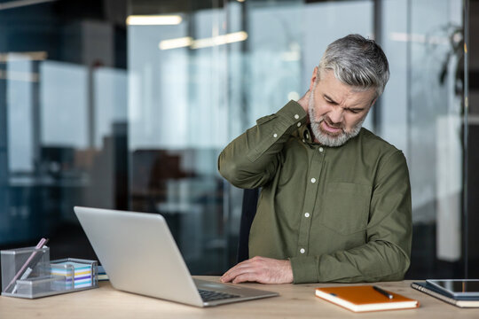 Mature man suffering neck pain working at office computer