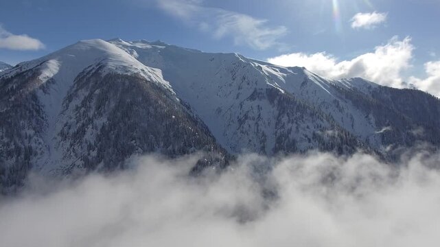 Aerial clouds drifting above snowy mountain ranges and deep alpine valleys in winter light. Layered vapor, icy summits, dramatic heights, cold wilderness, panoramic highland scenery.