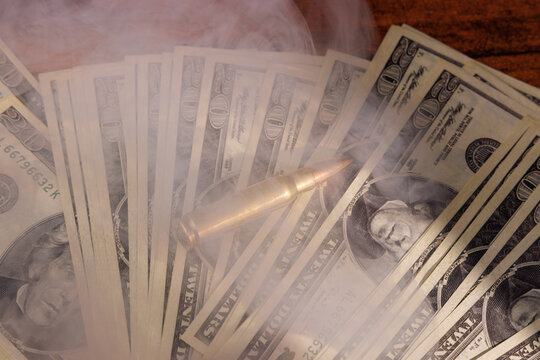 Stack of dollar bills beside rifle and handgun bullets on mahogany table representing the concepts of bribery and lethal threat.