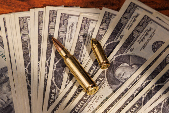 Twenty dollar cash stack with rifle and pistol bullets on mahogany wood surface representing the lethal nature of illegal greed.