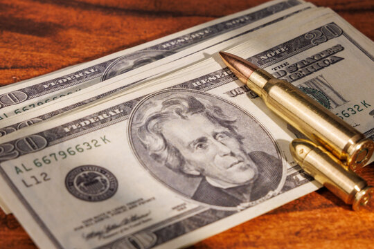 Twenty dollar bills next to lethal ammunition on mahogany table representing the dark side of wealth and the power of violence.
