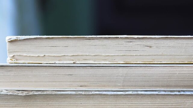 Taking away old vintage books one by one from a stack side view of yellowed paper edges and pages

