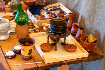 Collection of historical artifacts on a wooden table, small metal cauldron on a stand, clay oil...