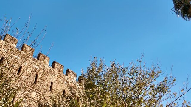 Ancient fortress merlons of antalya kaleici fortification with dry vegetation foreground on bright sunny day.