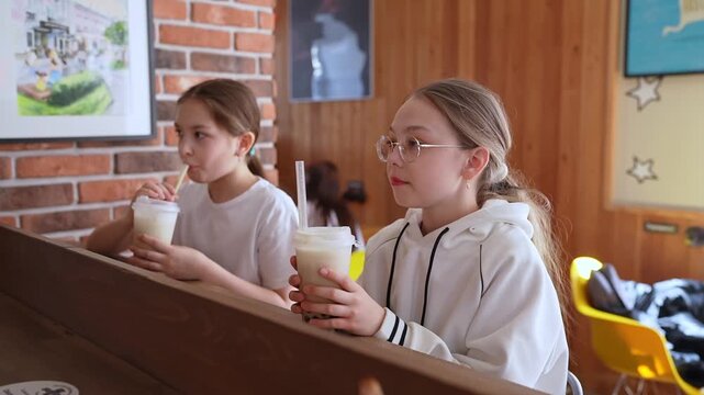 Friends in casual clothes sitting at high counter sipping bubble tea and smiling in modern cafe. Bubble tea, smiling, cafe, friends, counter.