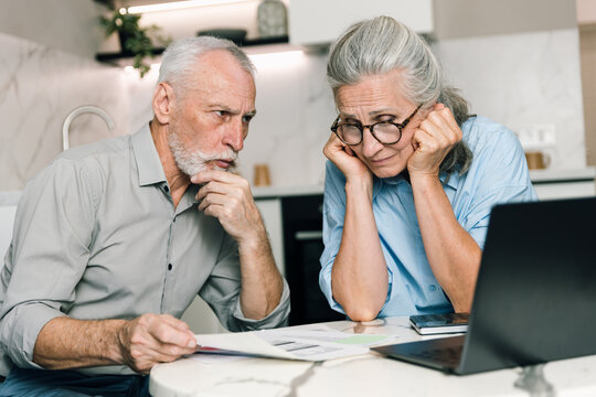 Elderly couple reviews bills and budgets on laptop at home in living space