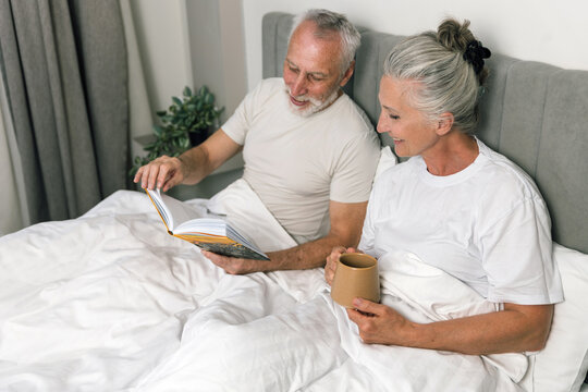 Senior couple happily reading book together in bed
