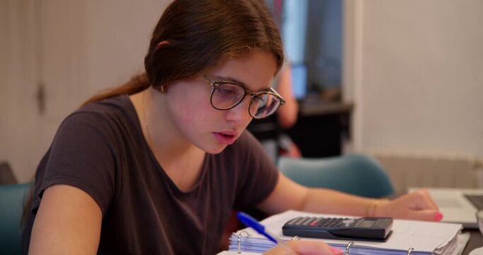 Focused study at Home: A student concentrates on her studies, with glasses, a pen, and a calculator at the ready. A study scene that evokes dedication and focus.