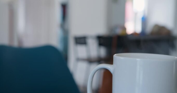 Morning Brew: A close-up shot of a pristine white ceramic mug, filled with a warm beverage, sits in a cozy living area, creating an atmosphere of comfort and relaxation. 