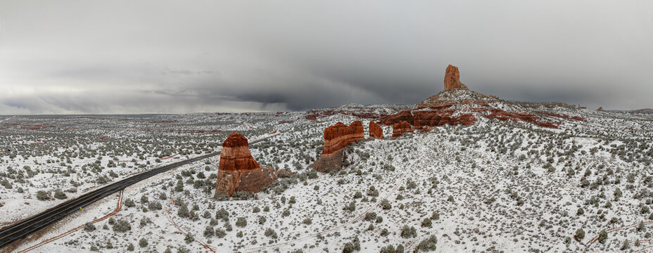 Aerial view of red rock buttes and a winding road in a snow-covered desert landscape under dark stormy clouds Page, Arizona, United States.