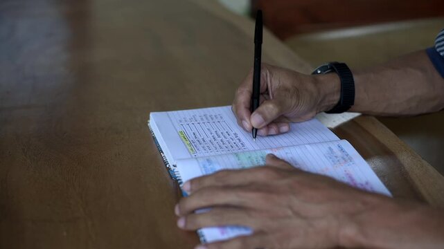 Asian male hand open book and writing on wooden table