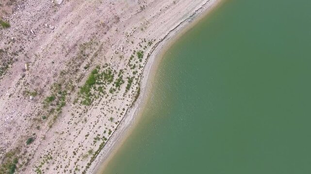 Aerial view shows evaporation lines along a coastline shaped by lake retreat and climate change. Receding water leaves stark patterns across the shore, reflecting global warming impacts.