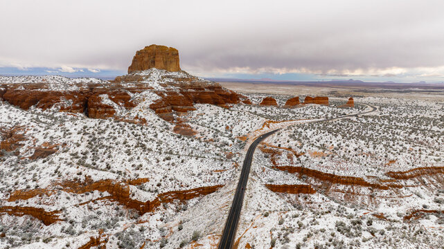 Aerial view of a majestic red rock mesa covered in fresh snow with a winding road through the desert landscape in Page, Arizona, United States.