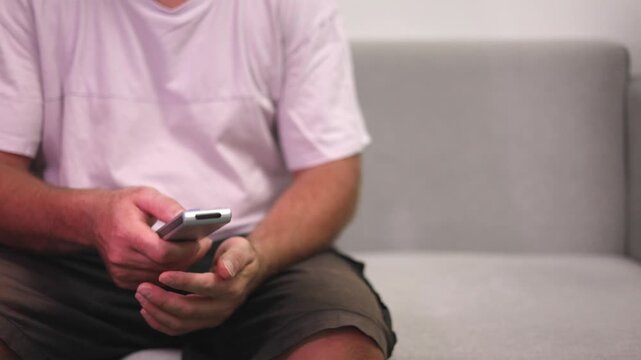 Person On Couch, Adult Sitting Comfortably Using Mobile Device, Person Reclining On Sofa Engaged With Phone Anxiously, Individual Relaxing On Sofa While Checking Messages With Nervous Anticipation