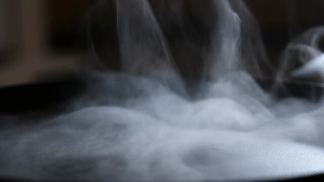 Slow motion static close up of steam rising and billowing from hot pan on kitchen stovetop during cooking with soft diffuse gray white vapor