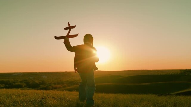 Girl kid aviator dreams flying becoming pilot. Little girl child wants become pilot astronaut. Slow motion. Happy child girl runs with toy airplane on field in sunset. Child play toy plane, sun sky
