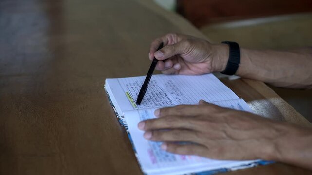 Asian male hand playing with a pen on book while thinking