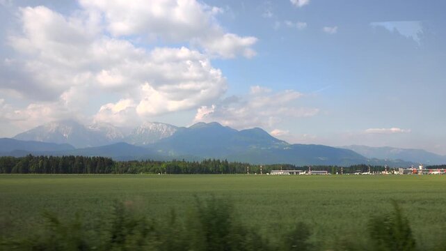 Departure view from Ljubljana airport runway across Slovenia countryside, fields and mountains. Takeoff scene near capital airfield, alpine horizon, blue sky clouds over rural landscape.