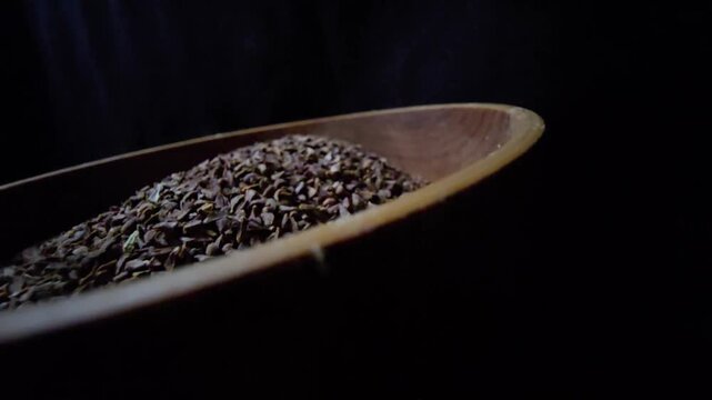 Close-up of dried Syrian Rue seeds (Peganum harmala) in a rustic wooden bowl, dark background, cinematic lighting, organic herbal texture.
