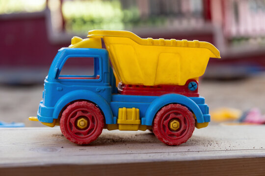 A colorful, well-worn plastic toy dump truck sits on a dusty outdoor surface at kindergarten.