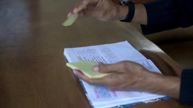 Asian male hand put yellow sticky note on book and want write on it