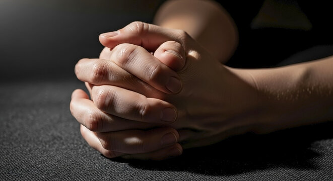 Hands clasped in grief with tightly interlocked fingers resting on soft surface. Hands in gesture of sadness and contemplation, expressing deep emotions.