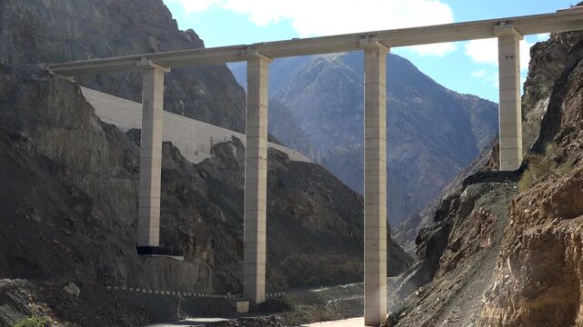 High concrete viaduct bridge and tunnel on mountain highway in Himalayas rocky valley. Dangerous elevated road span with pillars near cliff gorge, linking route to bore entrance.