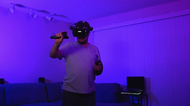 Man wearing virtual reality headset actively playing using controllers indoors interacting with virtual environment and immersing into modern gaming technology process