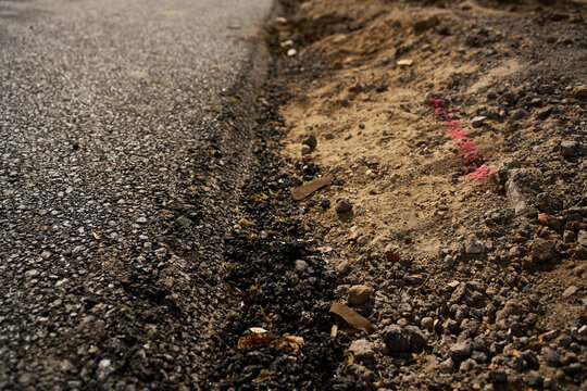 Road construction and groundwork. Black asphalt edge meeting a rough dirt and gravel shoulder.