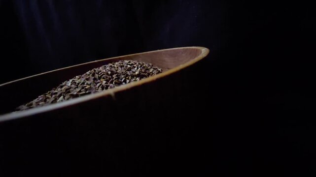 Close-up of dried Syrian Rue seeds (Peganum harmala) in a rustic wooden bowl, dark background, cinematic lighting, organic herbal texture.
