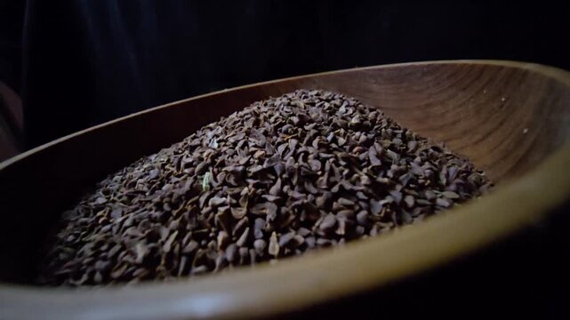Close-up of dried Syrian Rue seeds (Peganum harmala) in a rustic wooden bowl, dark background, cinematic lighting, organic herbal texture.