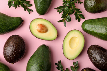 Naklejka premium Fresh ripe avocados and green leaves on pink background, flat lay