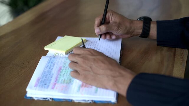 Asian male hand writing close up shot on book with yellow sticky note