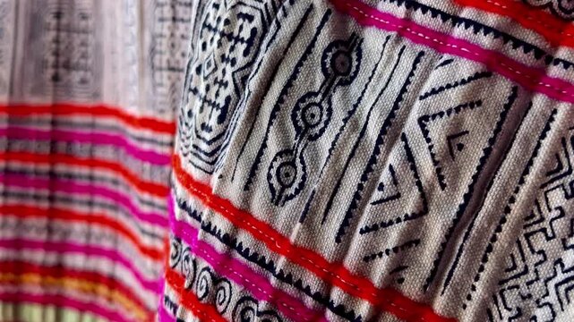 Close-up of an ancient embroidered textile with intricate ethnic patterns in vivid pink, red, and multicolor threads, showing fine craftsmanship, rich heritage, and textured folds in traditional fa
