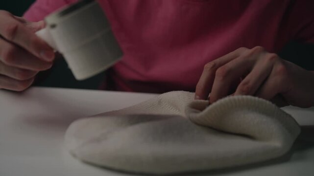 Person using electric lint remover machine on knitted beanie, demonstrating textile care and fabric restoration for renewed garment, close-up. Shooting in slow motion.