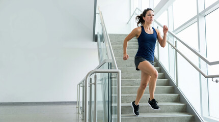 Obraz premium Fit woman sprinting up concrete stairs in a modern building. Female athlete in sportswear doing indoor cardio workout on staircase. Health and fitness training concept