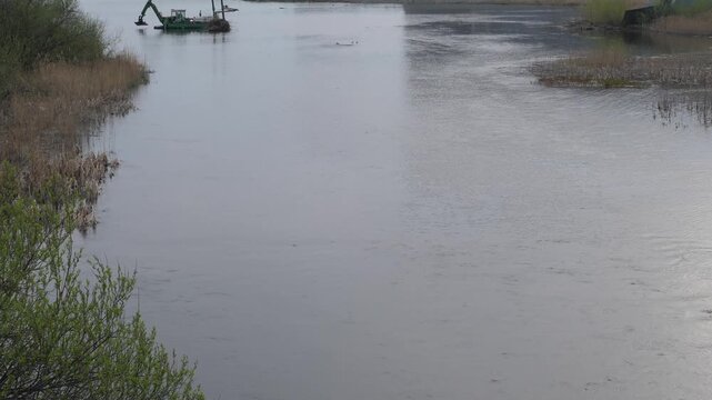 Multfunctional dredger performs cleaning and deepening works in the river bed. Dredging equipment parked near the riverbank on a cloudy spring day