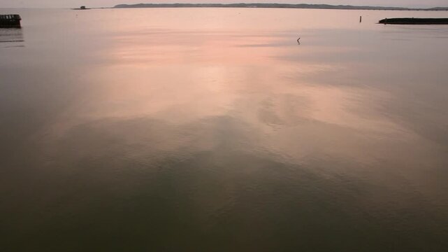 茨城県の霞ヶ浦、春の夕方に夕焼け空が静かな湖面へ映り込む湖畔のパーン映像