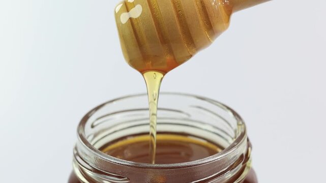 honey dripping from a wooden spoon on white background	