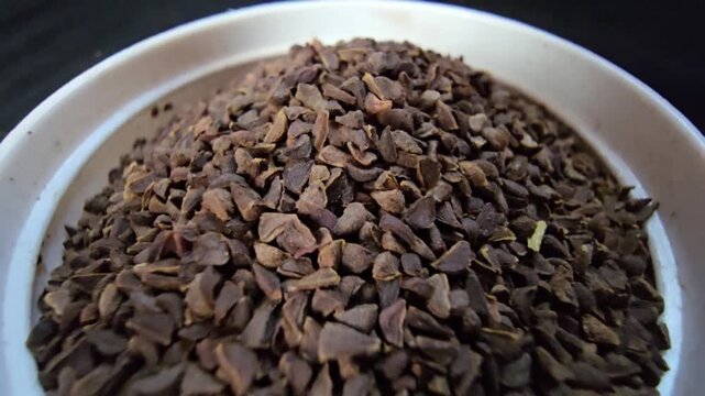 Extreme macro of Peganum harmala (Syrian Rue) seeds in a white bowl, detailed texture of herbal seeds used in traditional medicine and incense, dark background.