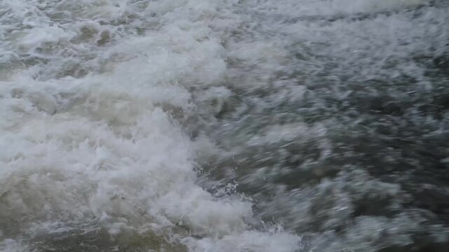 Churning river flow with intense white foam and strong current. Close-up of a powerful water cascade during spring flood.