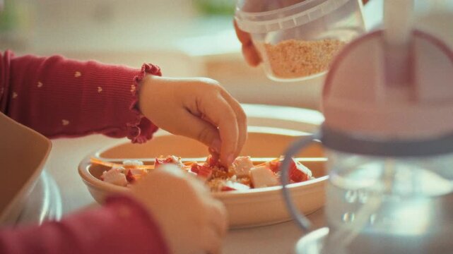 Curious child independently sprinkles sesame seeds onto their food, boosting flavor. This hands-on moment reflects early education and development, teaching youngster about seasoning and nutrition