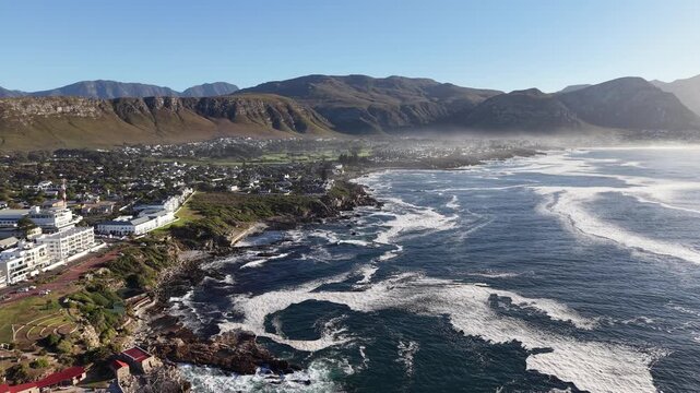 Hermanus, South Africa - January 19, 2026: Aerial drone view of Hermanus from the ocean, waves rolling along the coastline, clear blue sky and scenic seaside town in South Africa.