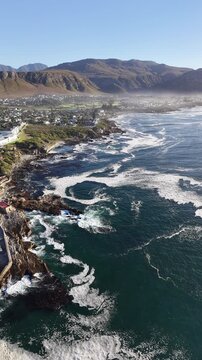 Hermanus, South Africa - January 19, 2026: Aerial drone view of Hermanus from the ocean, waves rolling along the coastline, clear blue sky and scenic seaside town in South Africa.