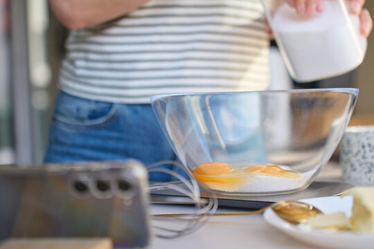 Eggs and sugar in glass bowl as person adds ingredient in kitchen